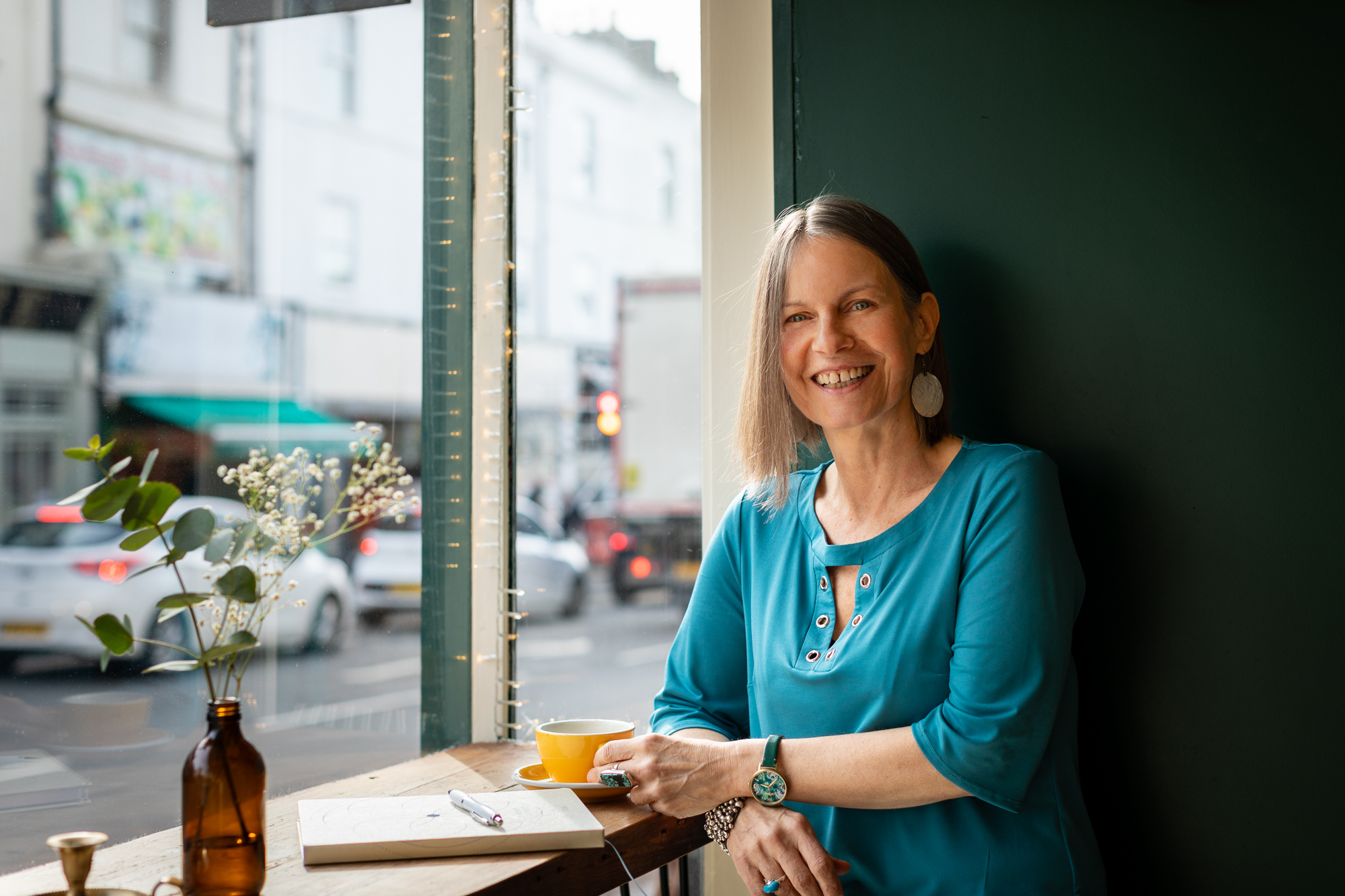Nicky Torode sitting at a cafe window with a notebook and coffee